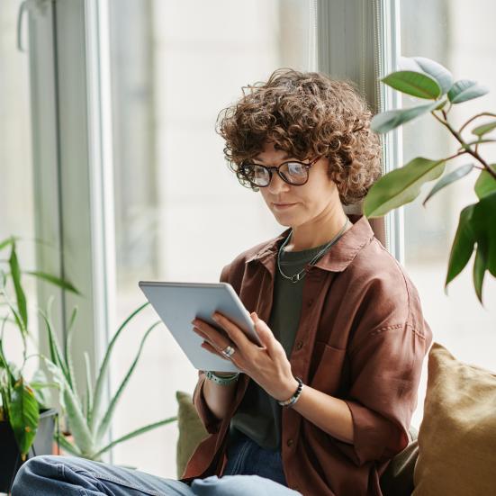 Kvinde, der sidder i en vindueskarm og læser på en tablet.