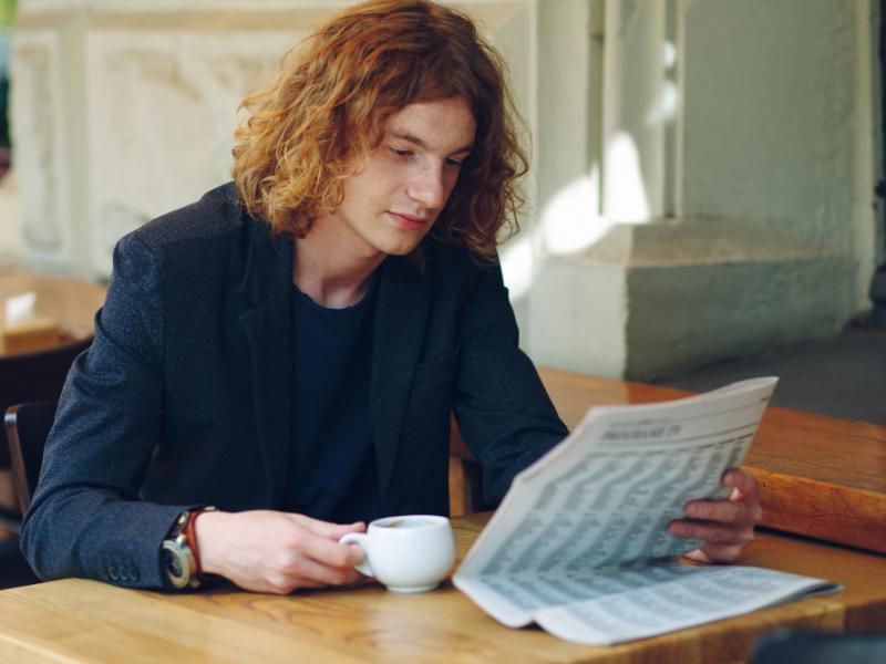 Mand, der sidder på en café og læser en avis, mens han drikker en kop kaffe.