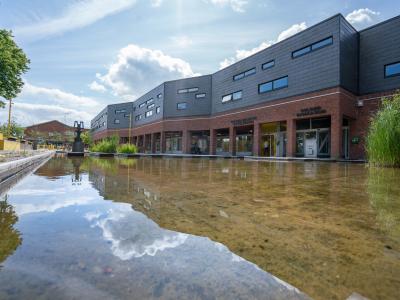 Bibliotekets facade. I forgrunden ses vandspejlet ved indgangen. Midt i billedet ses Solrød Bibliotek og Kulturhus, med sine røde mursten i stueetagen, og den blanke, mørkegrå front på første sal.