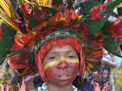 Fotografi af lokal person fra Papua New Guinea iført farvestrålende ansigstmaling og hovedbeklædning med fjer. 
