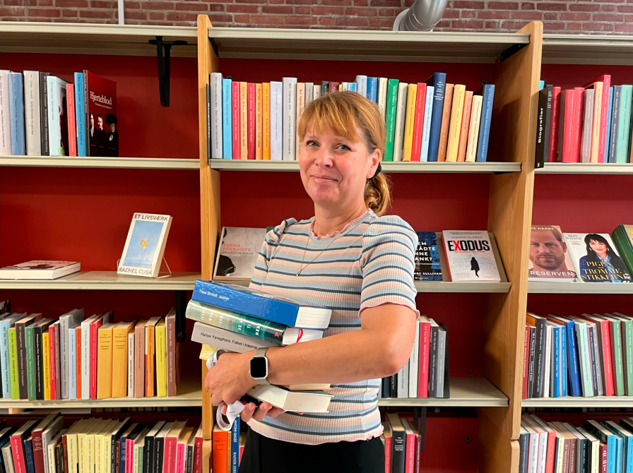 Pia Brun Jepsen, der holder en stak bøger. Hun står foran en bogreol ude i biblioteket.